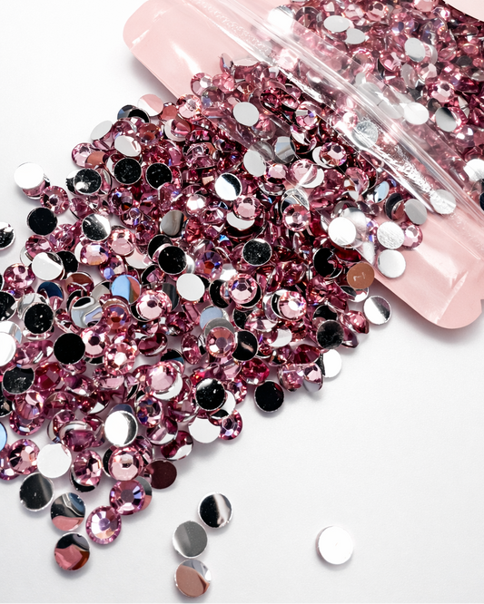Pink rhinestones spilling out of a pink packaging container on a white background